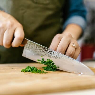 Person cutting parsley on cutting board with Damascus knife