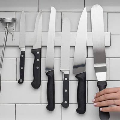 Magnetic knife holder on kitchen wall with knives attached