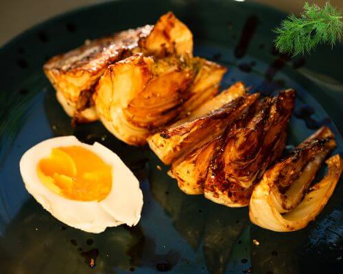 Roasted fennel slices with half boiled egg on plate