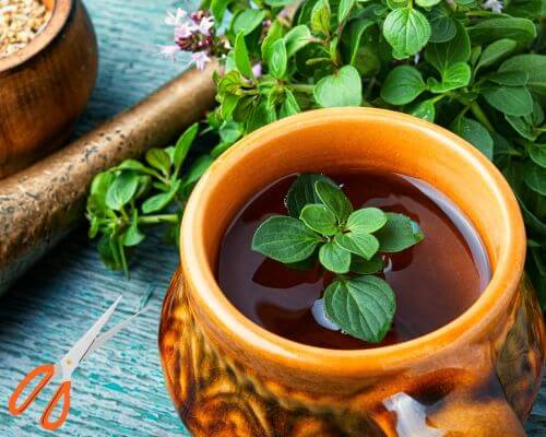 A cup of oregano tea with background of mortar/pestle and green oregano