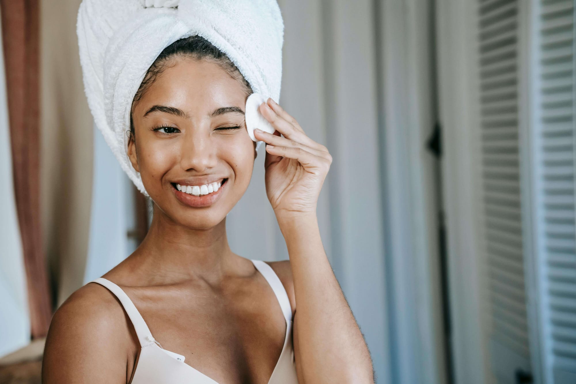 Woman with towel around hair holding a pad gently rubbing face with it